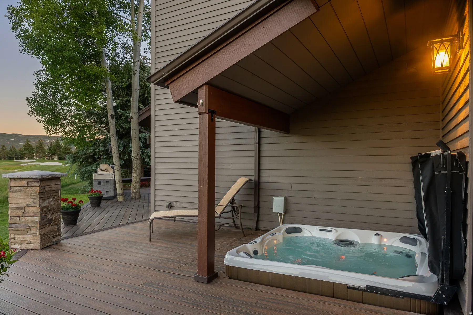 Outdoor deck featuring a hot tub, covered patio area, and stone-clad column