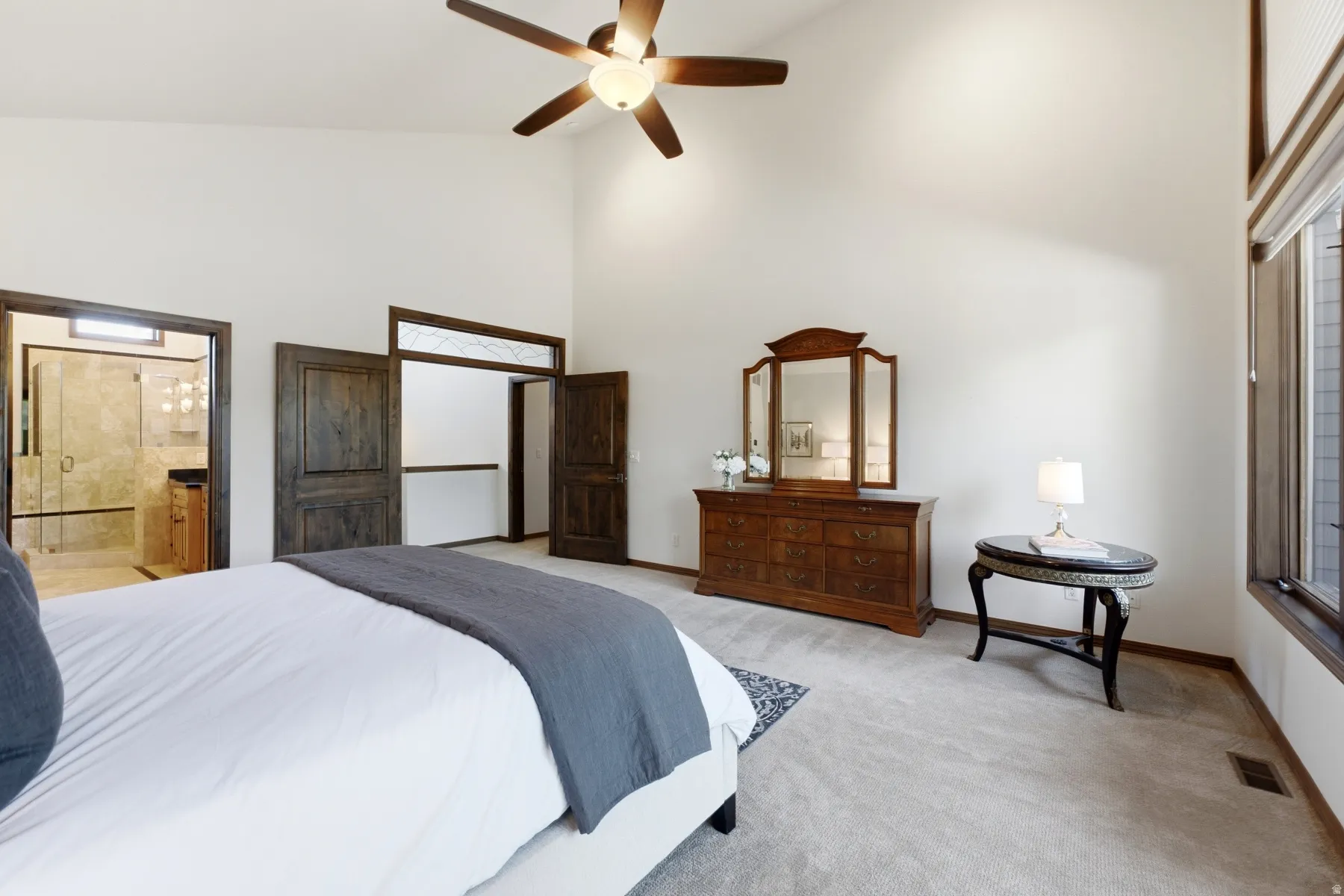 Vaulted ceiling with a ceiling fan, carpet flooring, large windows, and a bathroom entrance featuring a glass-enclosed shower