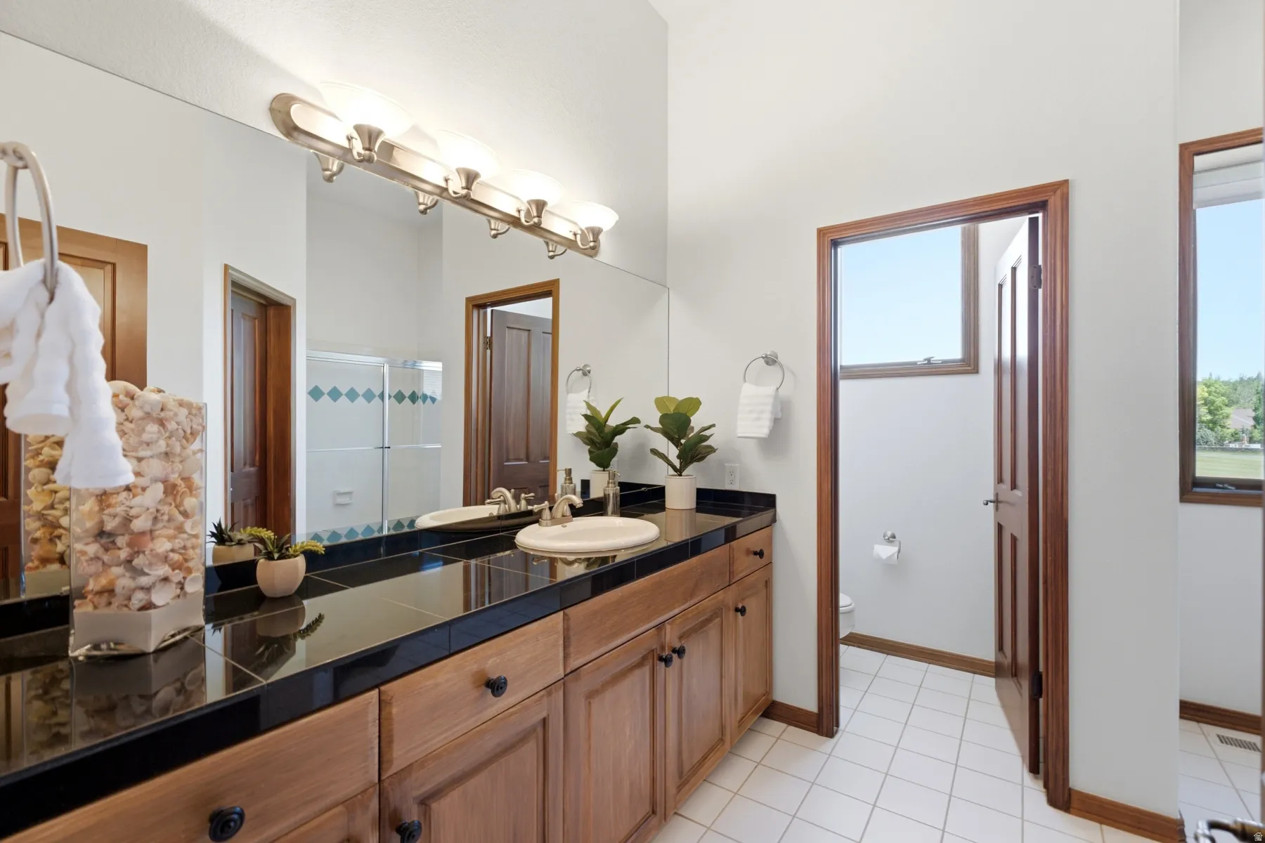 Double vanity with wood-finish cabinetry, black tile countertop, and undermount sinks