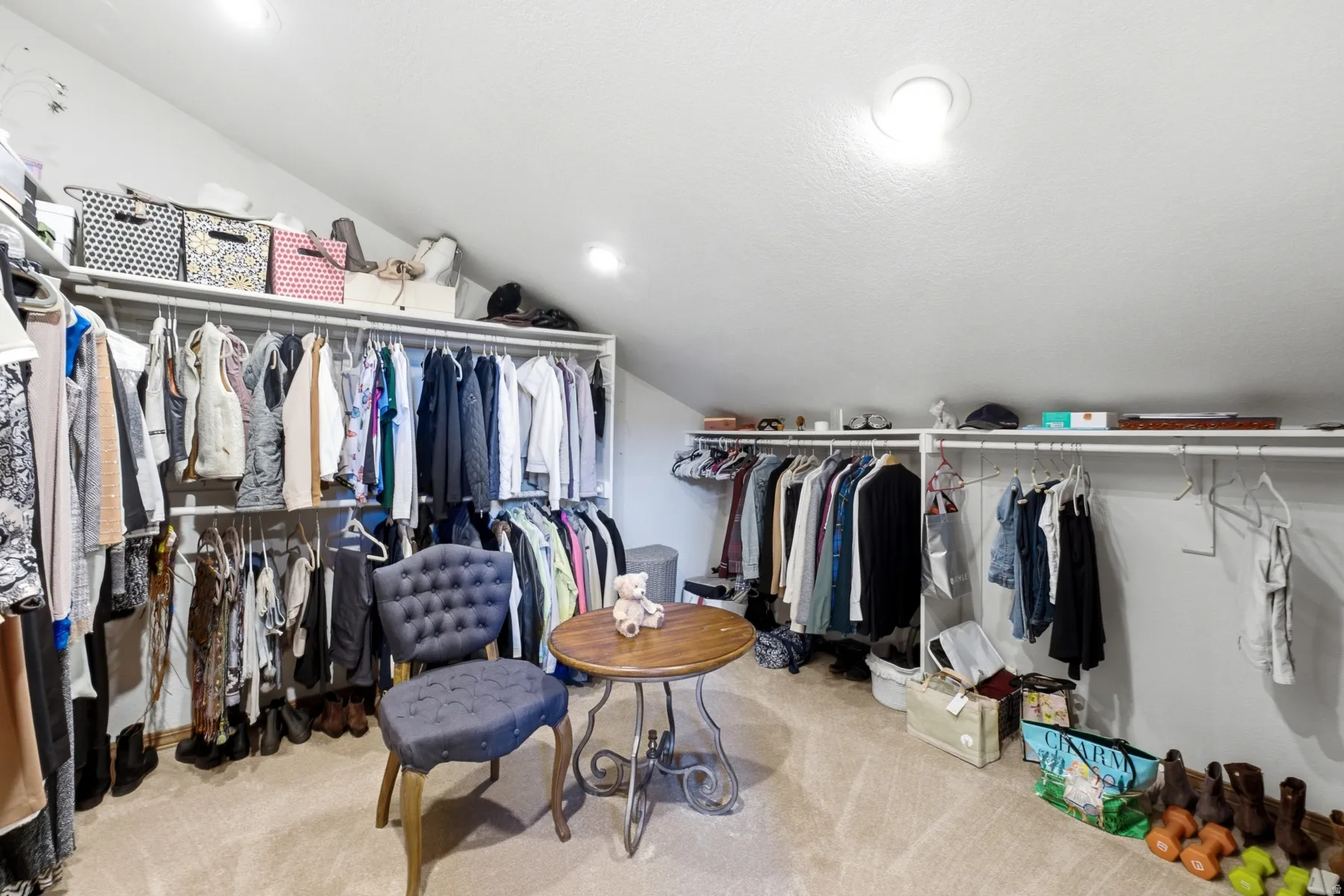 Spacious attic conversion featuring sloped ceilings, recessed lighting, wall-mounted clothing rods, and built-in shelving for organized storage