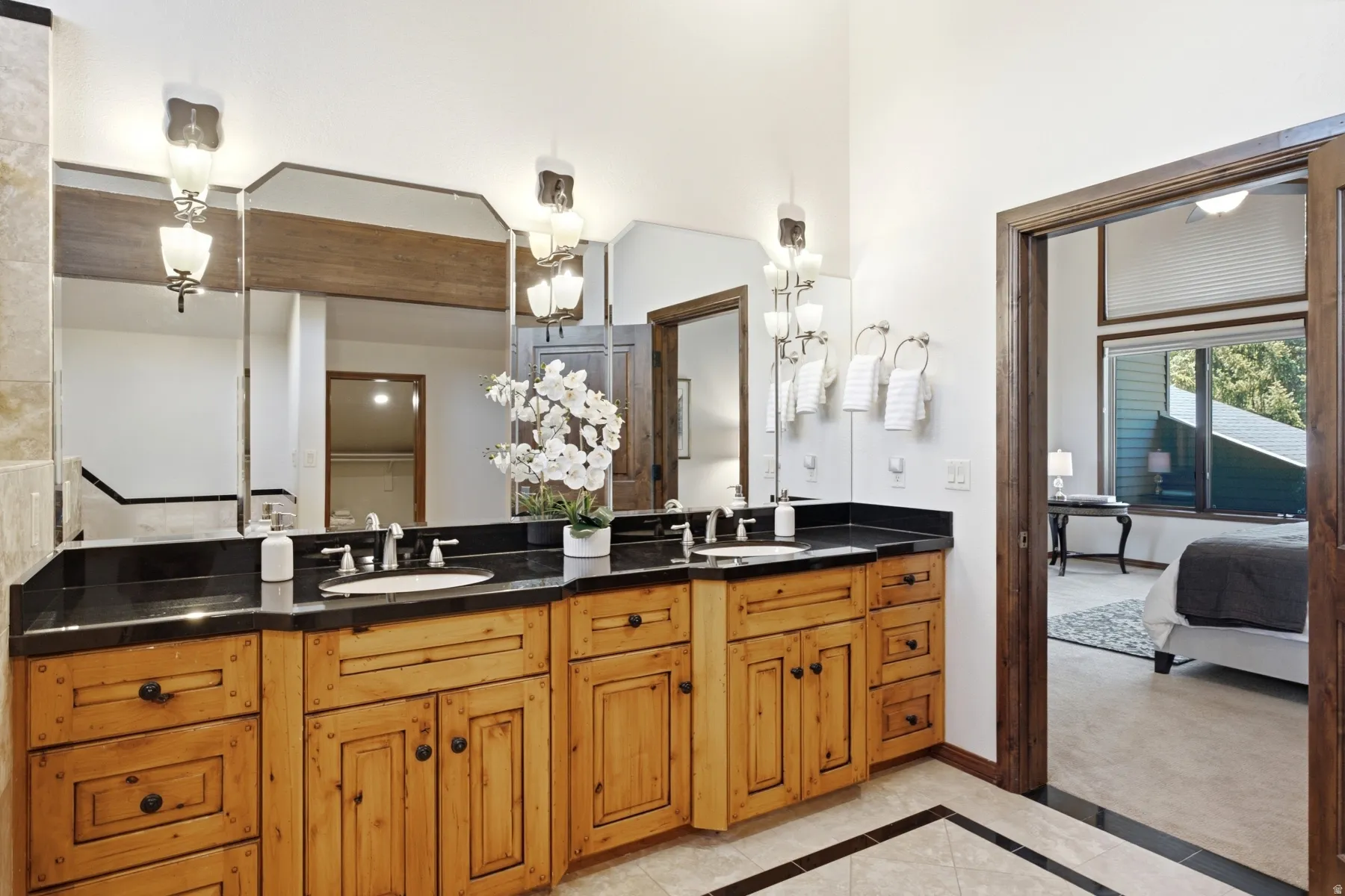 Dual basin vanity featuring wood cabinetry, dark countertops, and integrated mirrors with sconce lighting