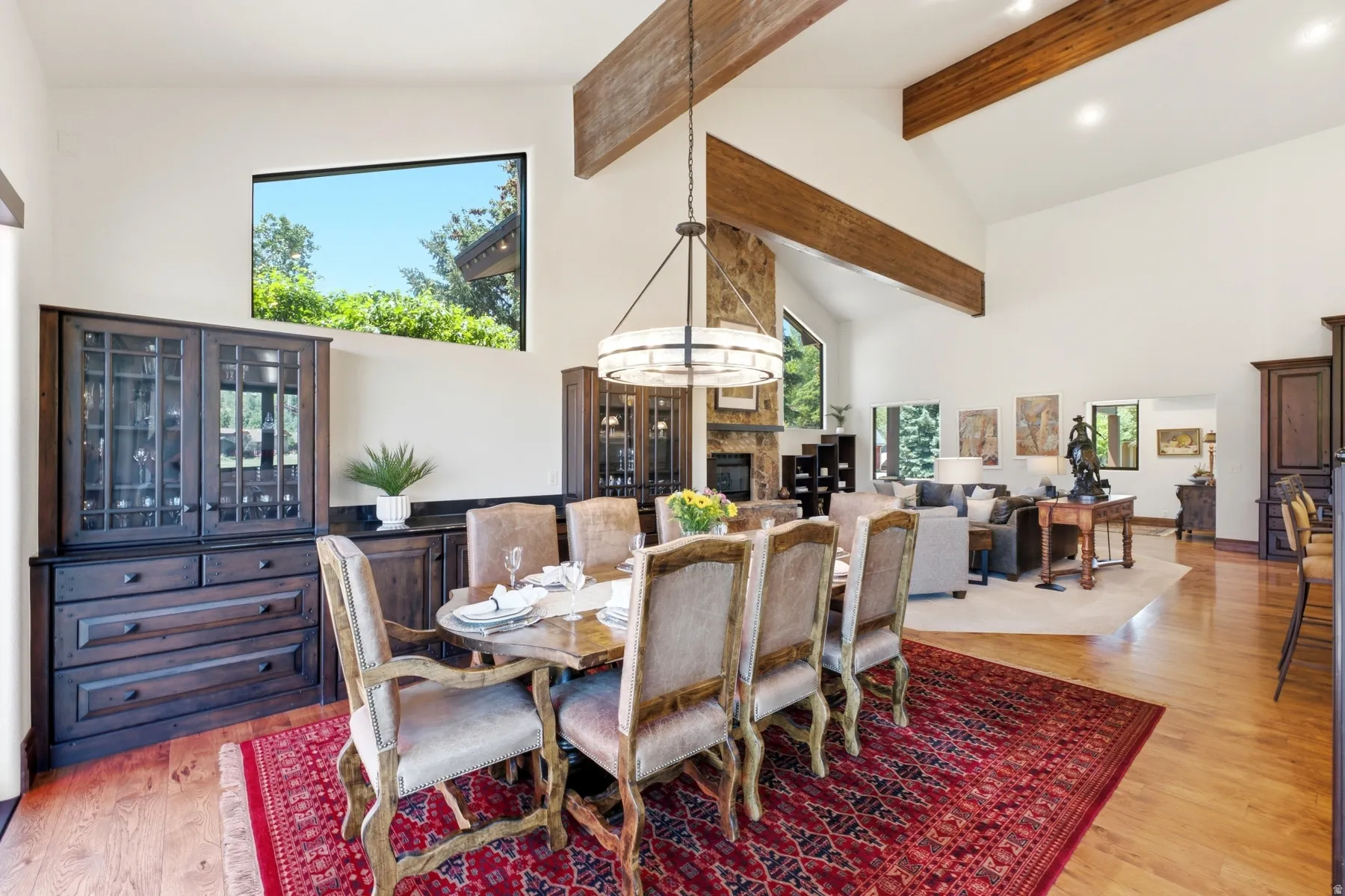 Dining area featuring high vaulted ceilings with exposed wood beams, a contemporary chandelier, hardwood flooring, and a large rectangular window