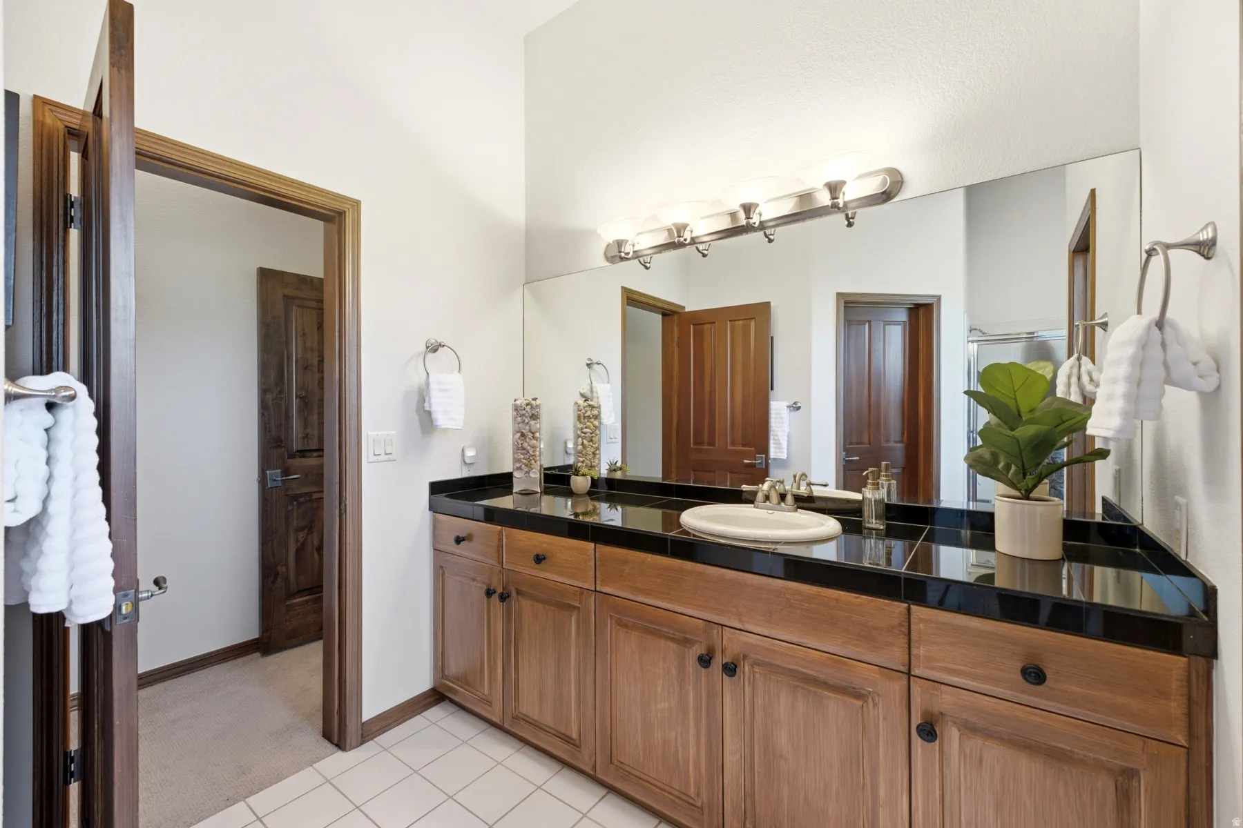 Vanity featuring wood cabinetry with black hardware, a black tile countertop, and an oval undermount sink with a chrome faucet