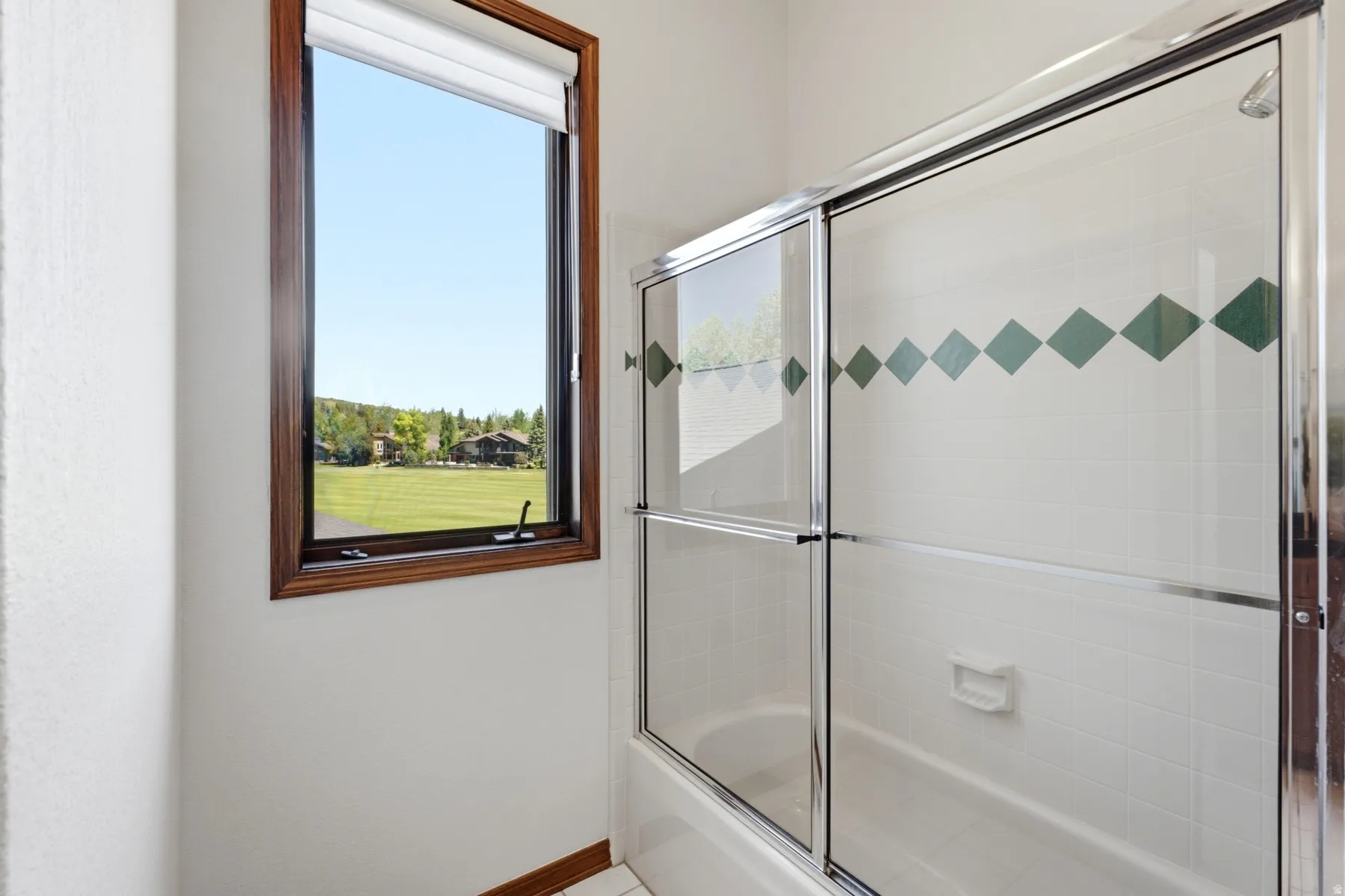 Alcove bathtub with sliding glass enclosure featuring decorative green tile accents