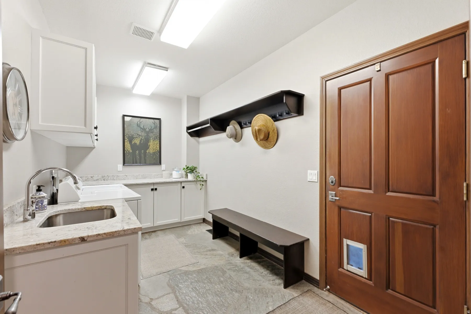 Utility room featuring a stainless steel sink, granite countertops, white cabinetry, slate tile flooring, and a wood-paneled door