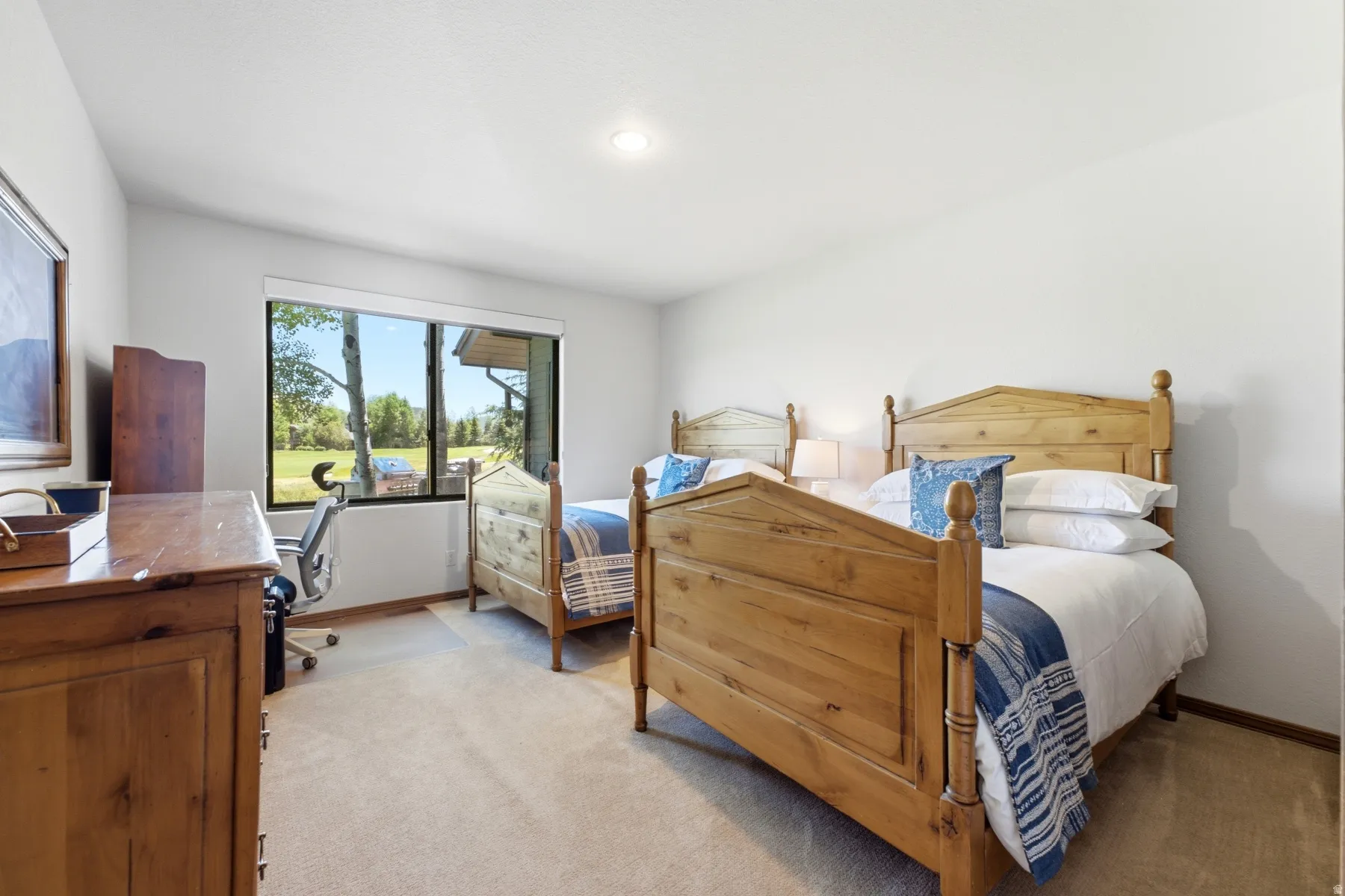 Carpeted room with two wooden bed frames, a large window, and a light-colored wall