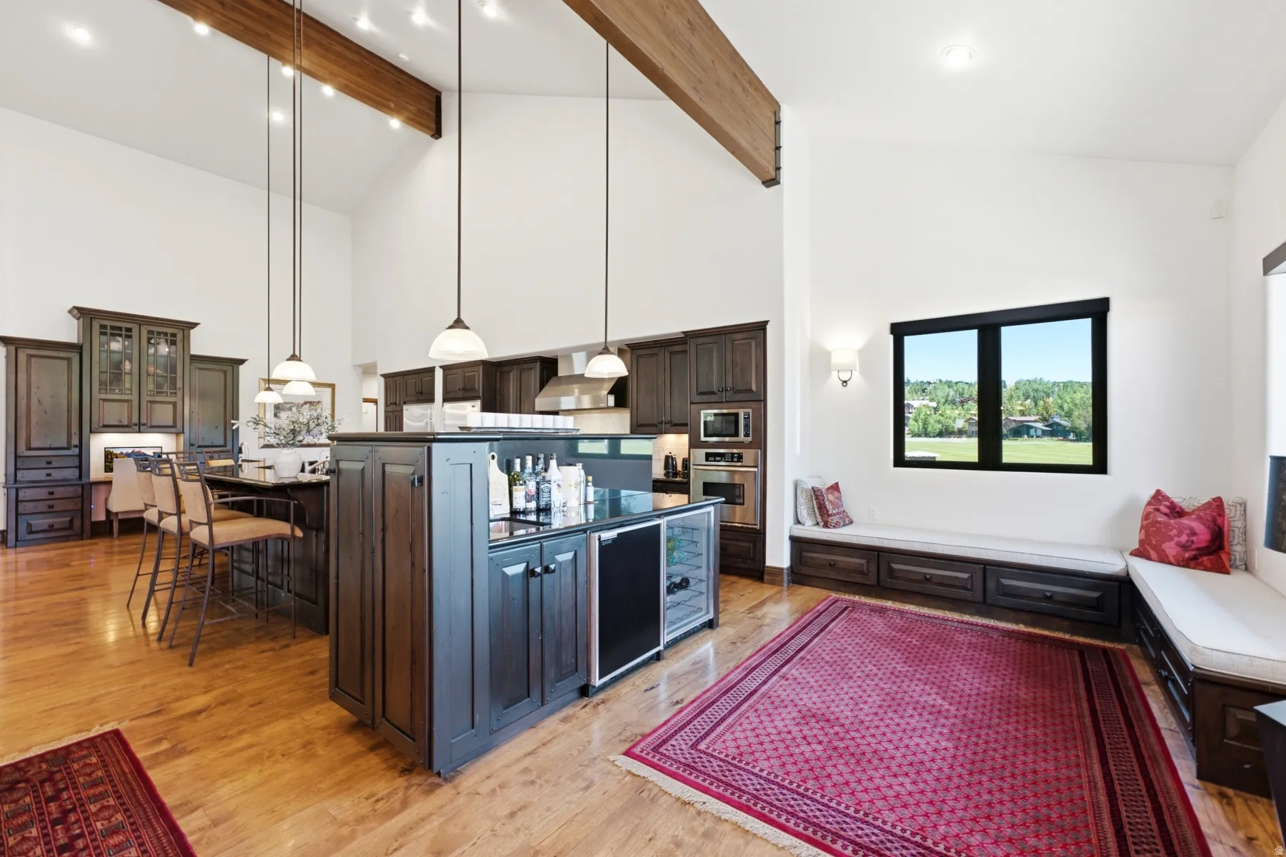 Spacious kitchen and living area featuring high vaulted ceilings with exposed wood beams, hardwood flooring, and dark wood cabinetry