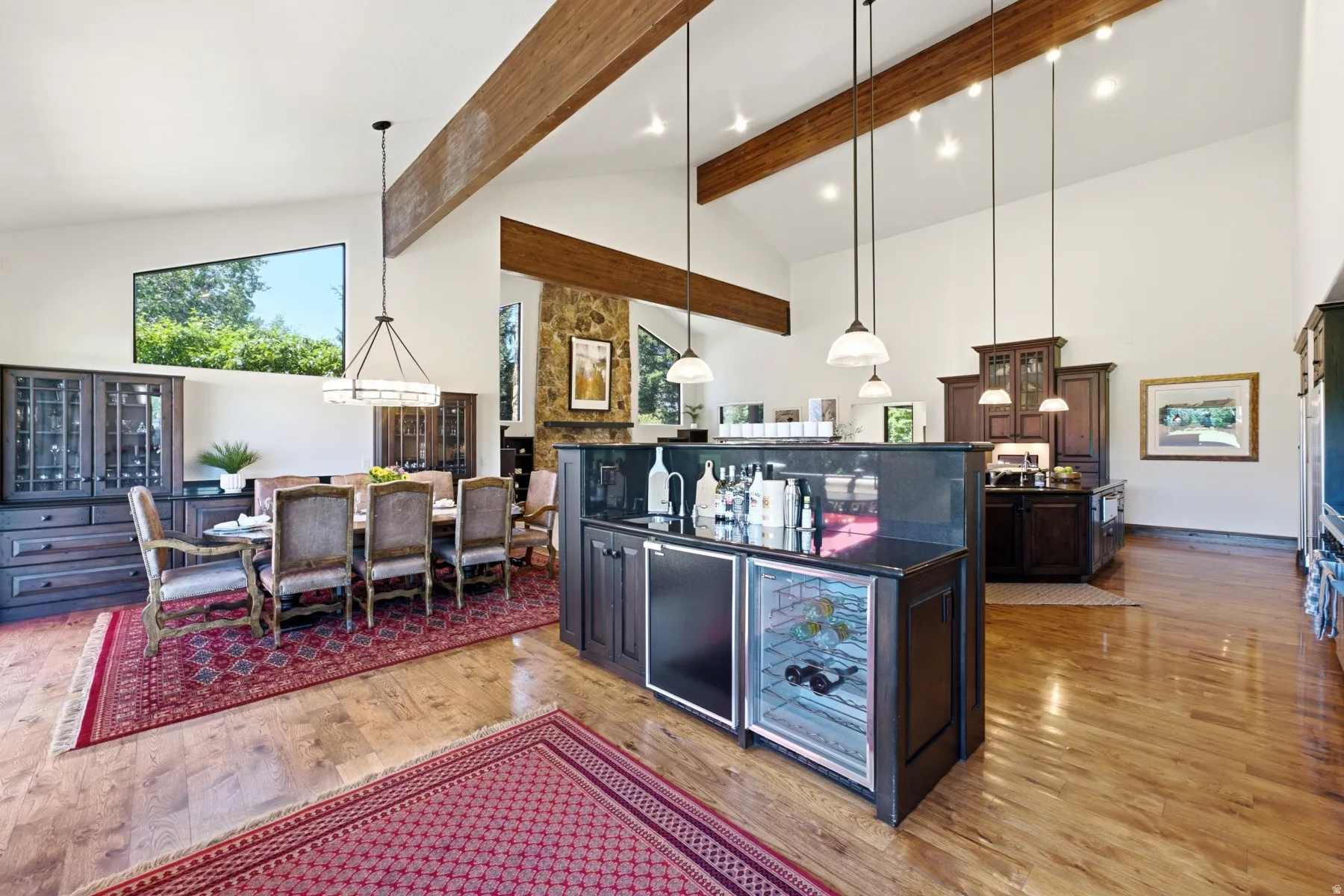 Vaulted ceilings with exposed wood beams, wood-finish flooring, and a stone-clad fireplace