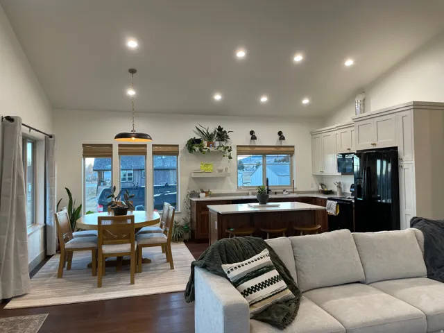 Open-concept living space featuring vaulted ceilings, recessed lighting, wood-finish flooring, a kitchen island with seating, and light-toned cabinetry