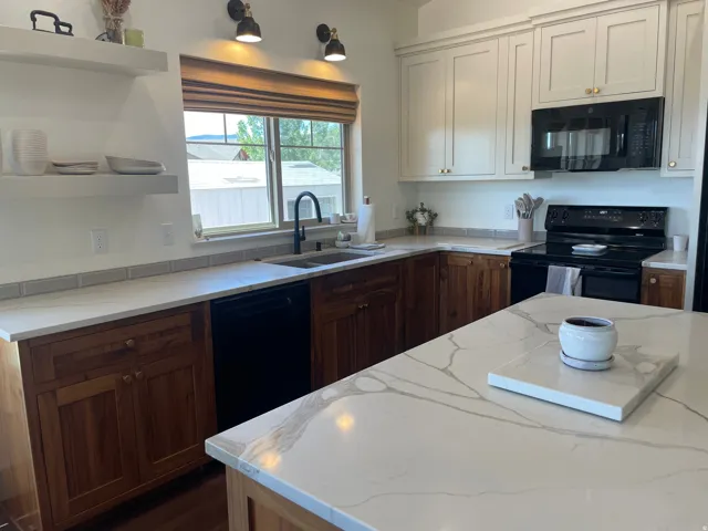 Kitchen featuring white cabinetry and wood-finish lower cabinets, stone-finish countertops, a black appliance suite, and a large central island