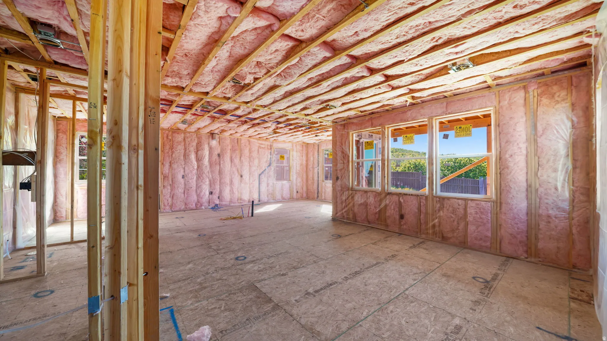 Interior framing with exposed wood studs, insulated walls and ceiling, rough plywood subfloor, and multiple windows
