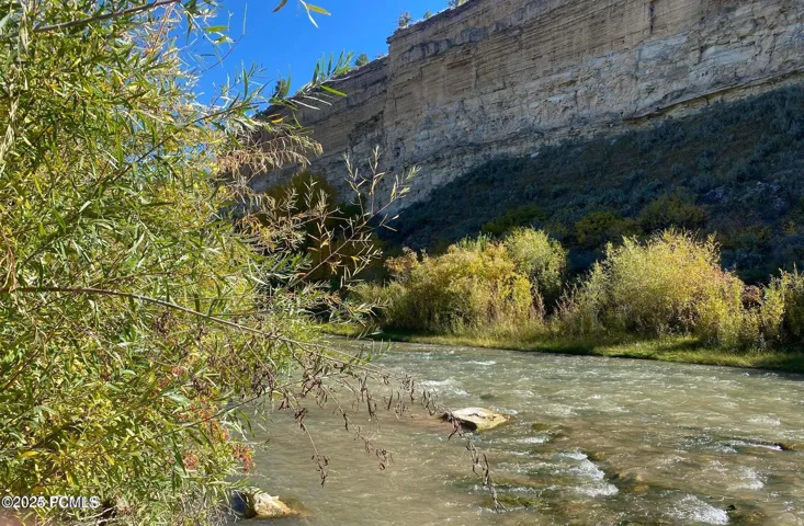 Riverfront property featuring natural rock formations, lush vegetation, and a clear blue sky overhead