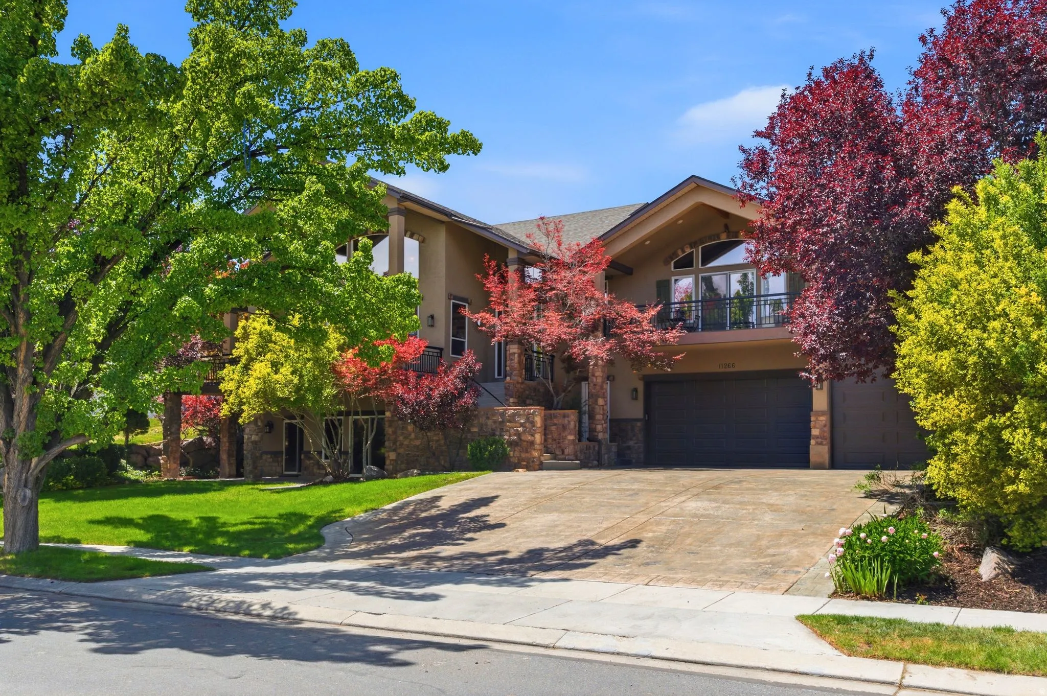 Contemporary residence featuring a stucco and stone facade, expansive driveway, attached garage, and a second-story balcony with an arched window
