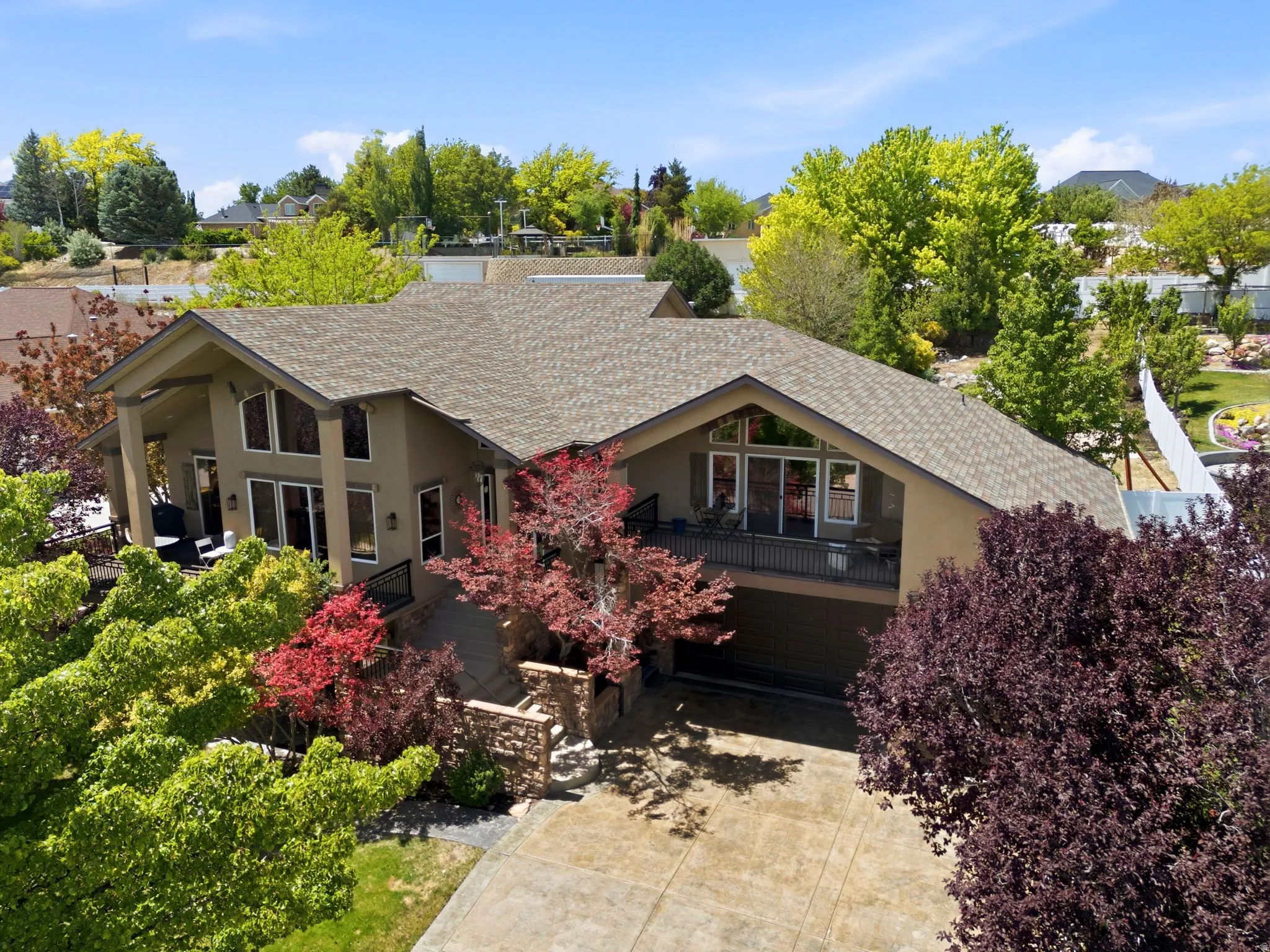 Contemporary home featuring a stucco exterior with an attached garage, a second-story balcony with metal railings, a covered patio, and extensive landscaping