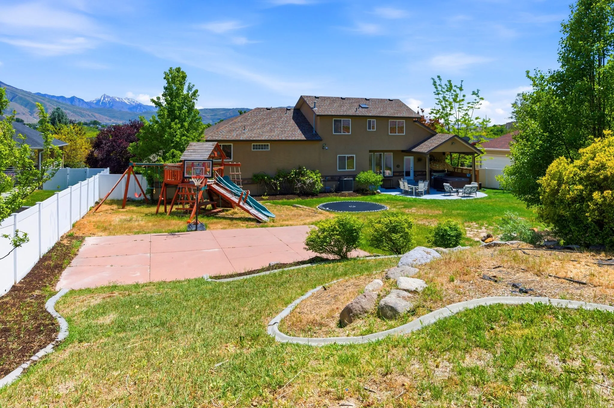 Expansive backyard featuring a covered patio, concrete sports court, and a white vinyl fence