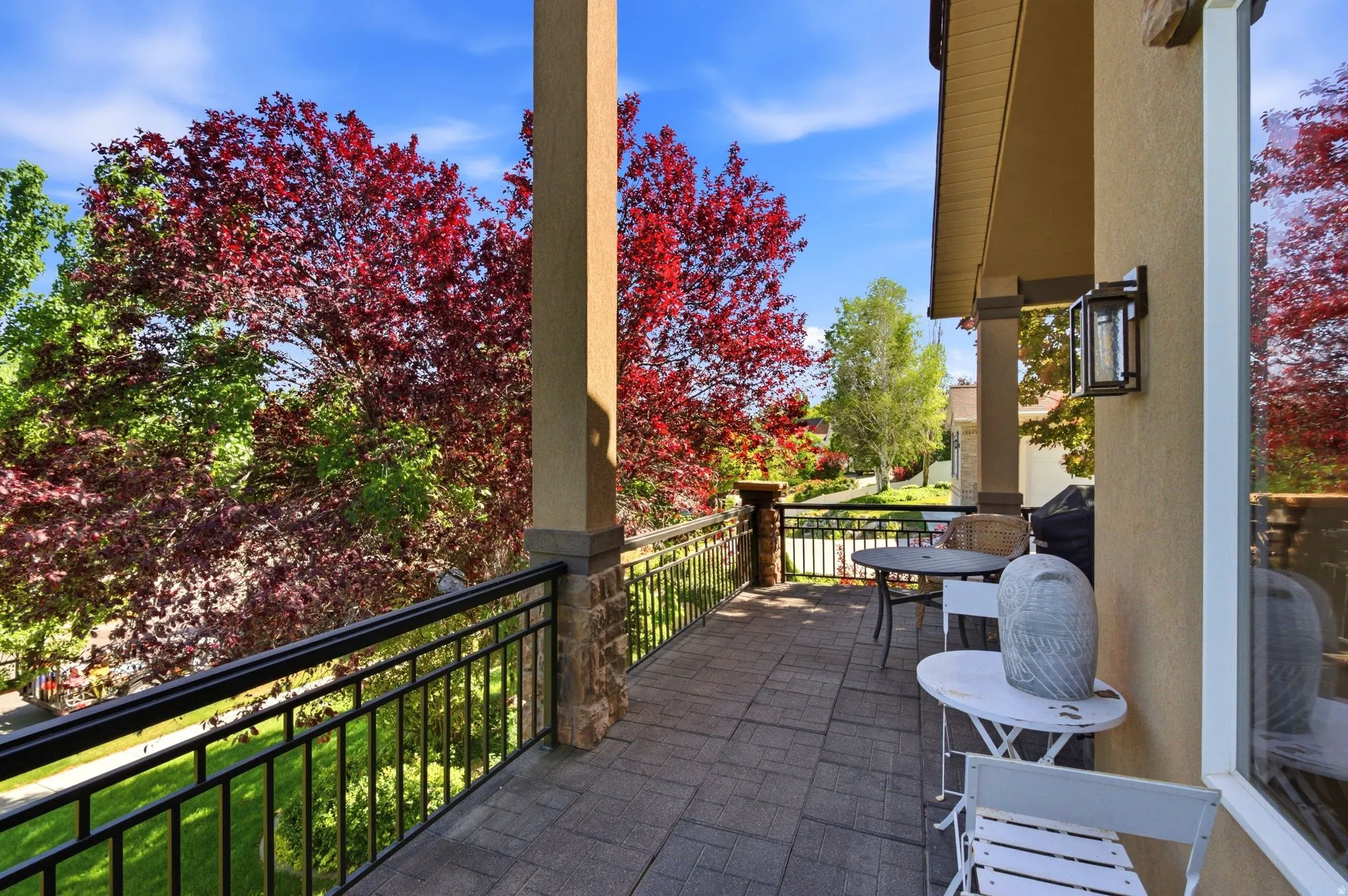 Spacious covered patio with a paver tile surface, decorative metal railing, and stone-clad pillars