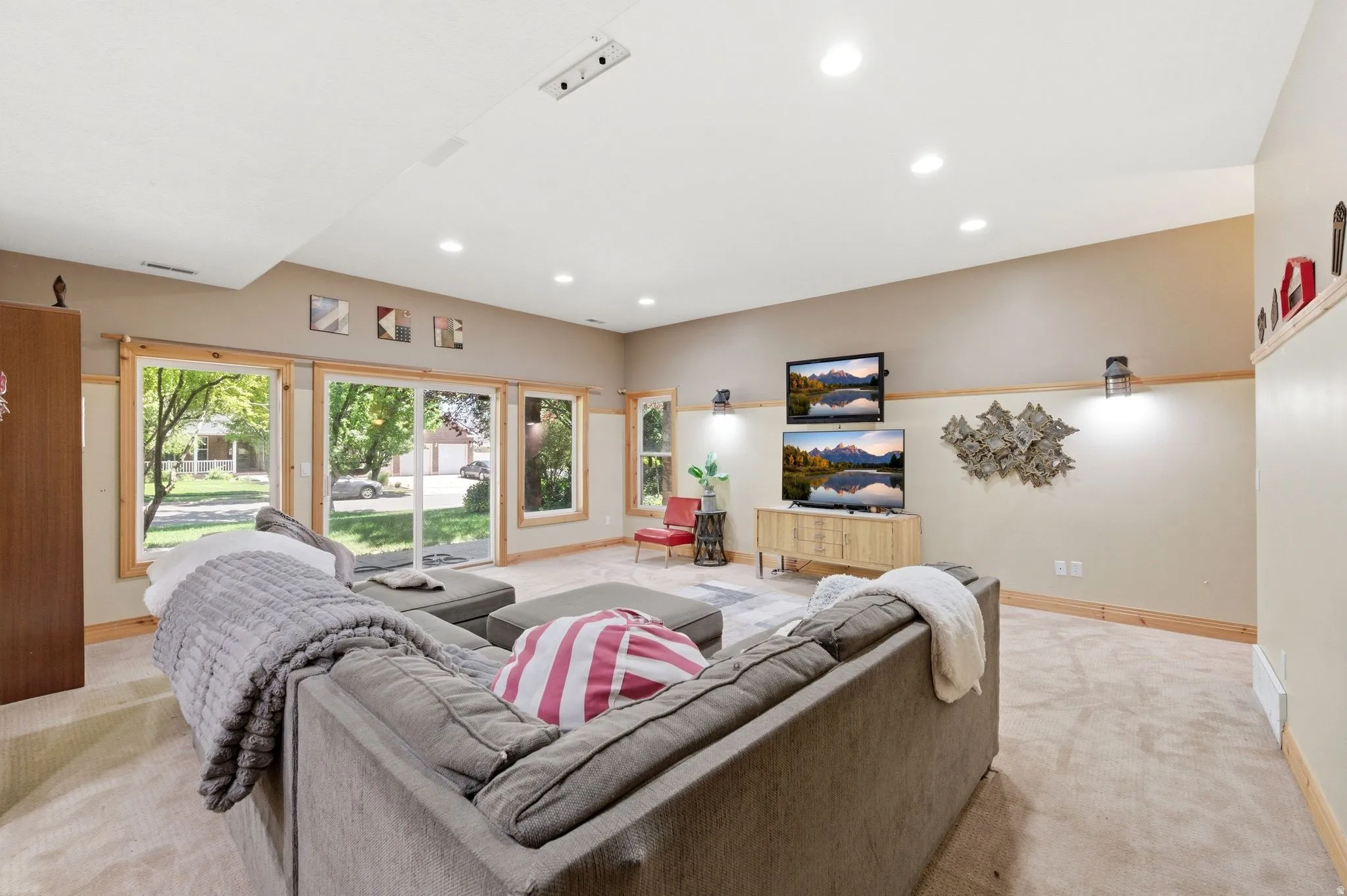 Expansive entertainment space featuring recessed lighting, a sliding glass door, multiple windows with wood-finish trim, and wall-mounted sconces