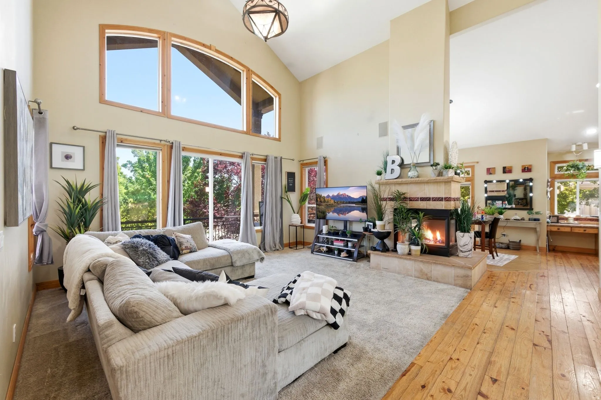 Vaulted living space featuring a tiled fireplace, wood-finish flooring, and expansive windows