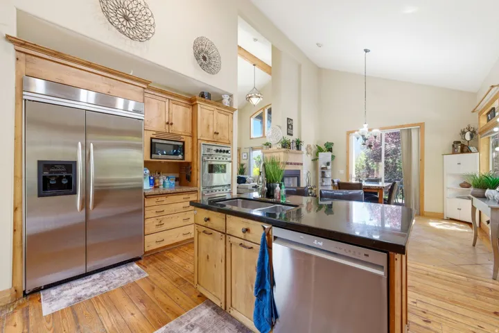 Spacious kitchen featuring an expansive island with a built-in sink and stainless steel dishwasher, ample wood cabinetry, integrated stainless steel appliances, and wood-finish flooring