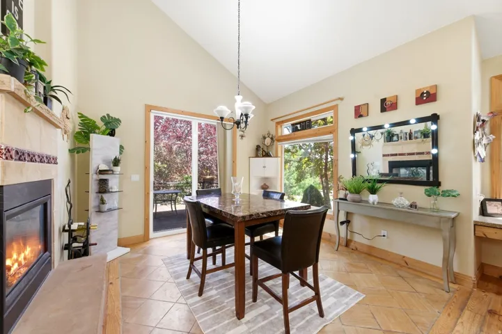 Spacious dining area featuring vaulted ceilings, tile flooring, a built-in fireplace with a tiled surround, a sliding glass door to the exterior, and large windows with natural wood trim