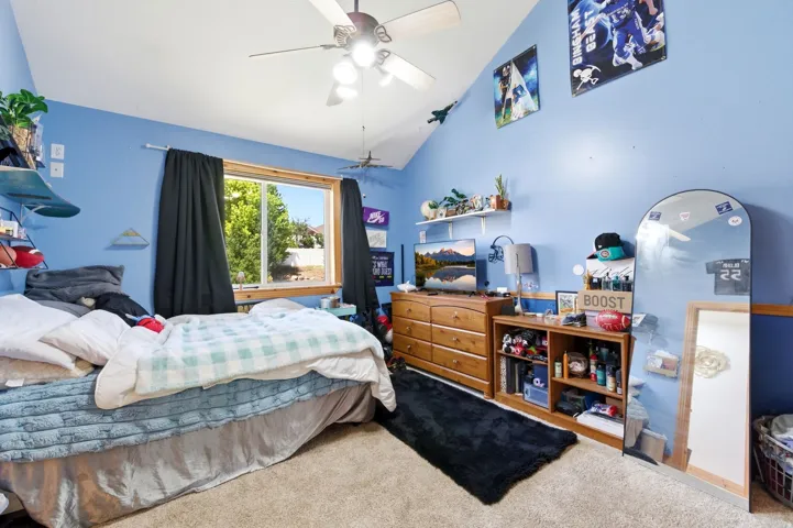Carpeted room featuring a ceiling fan, sloped ceiling, and a large window with black-out curtains