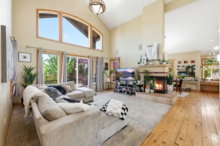 Vaulted living space featuring a tiled fireplace, wood-finish flooring, and expansive windows