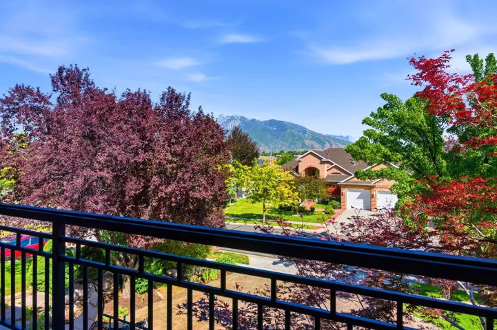 Balcony featuring black wrought iron railing, mature trees with varied foliage, and distant mountain scenery