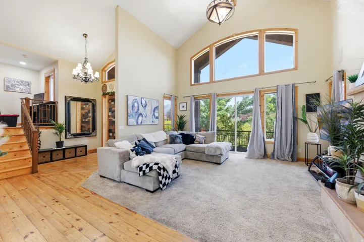 Spacious living area featuring a vaulted ceiling, large arched windows, and a sliding glass door opening to an outdoor balcony
