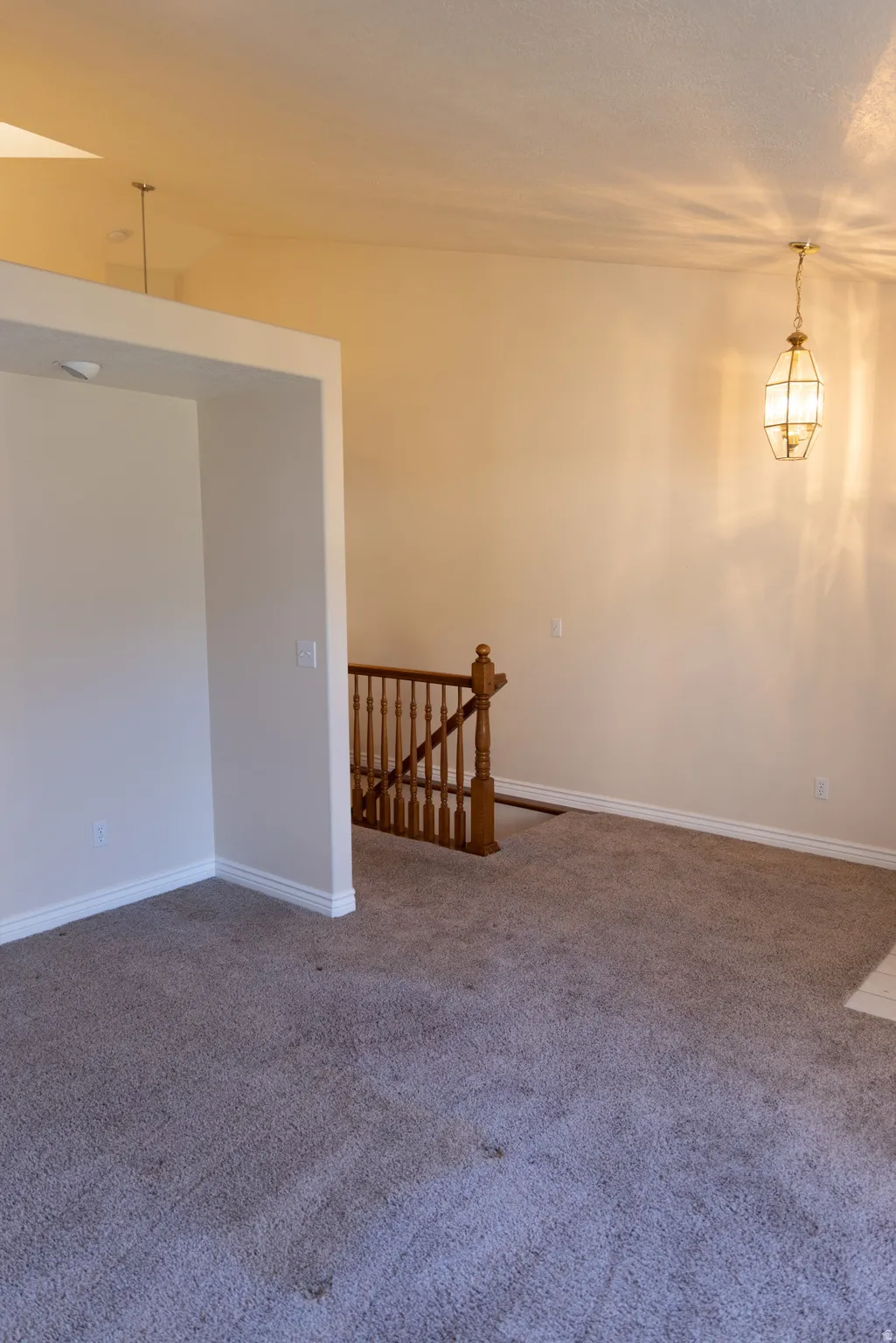 Carpeted living area with vaulted ceilings, a decorative pendant light fixture, and a wood banister