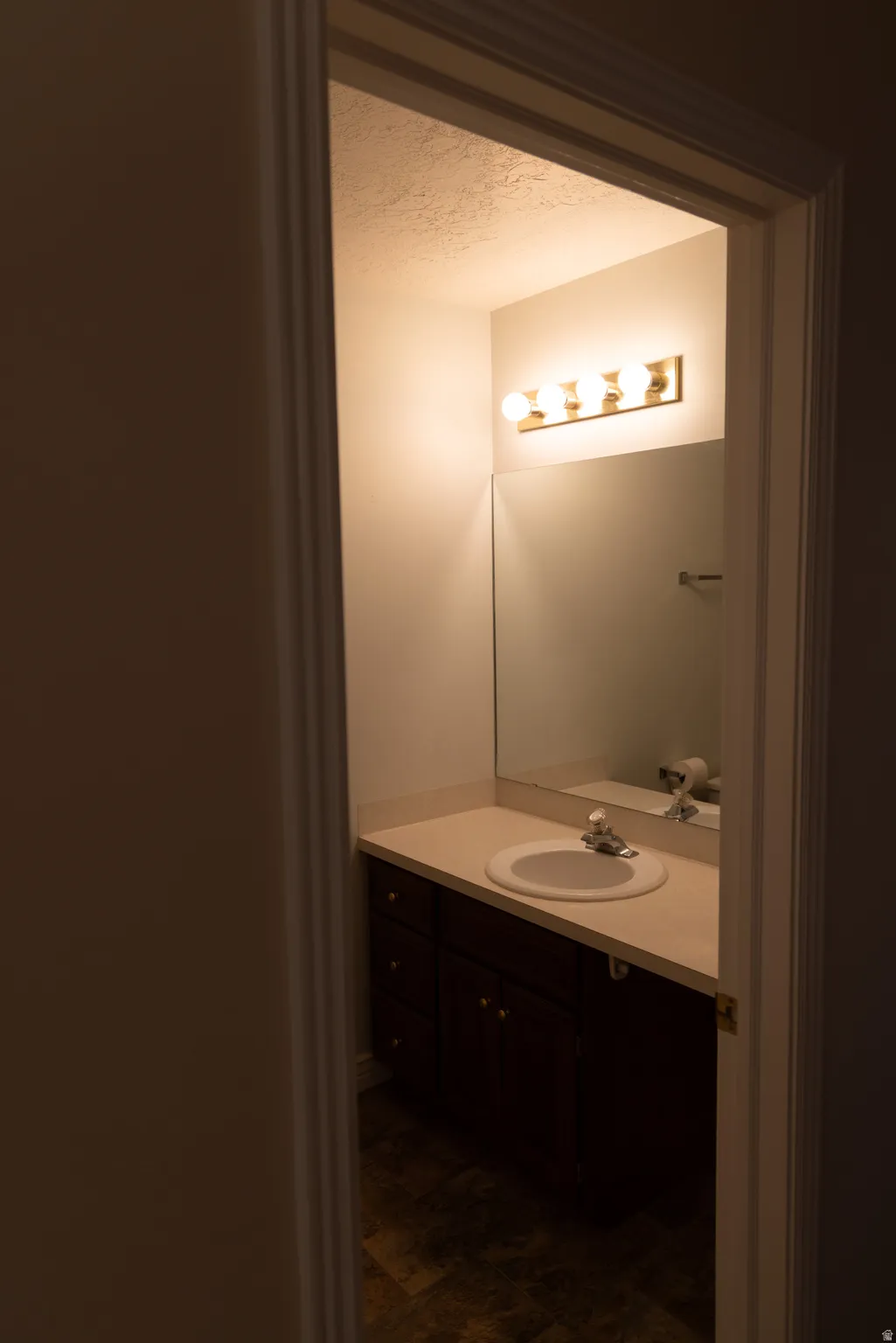 Bathroom vanity featuring a light-toned countertop with integrated sink, a dark wood-finish cabinet, a large wall-mounted mirror, and a four-bulb vanity light fixture