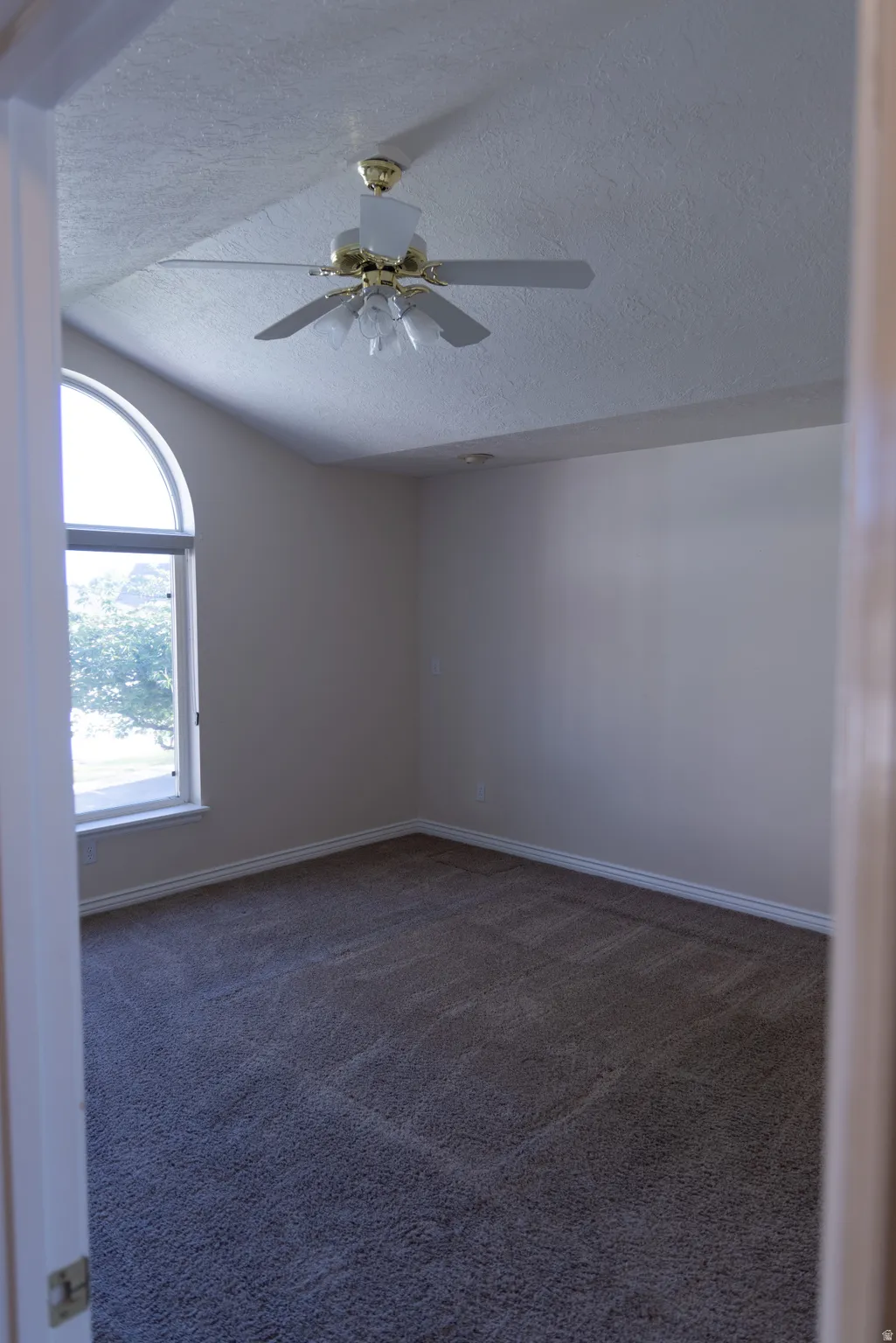 Room featuring vaulted ceiling, arched window, wall-to-wall carpeting, and a ceiling fan with integrated lighting