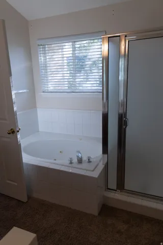 Tiled corner soaking tub with integrated jets and chrome fixtures, accompanied by a glass-enclosed shower with a sliding door