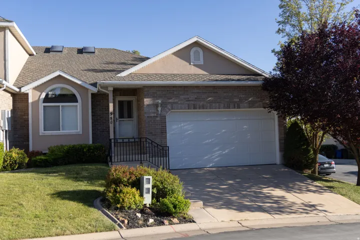 Brick and stucco exterior with an attached garage, paved driveway, and front entry with wrought iron railing
