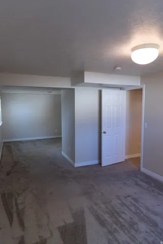 Spacious room featuring gray carpet flooring, white baseboards, a white interior door, and a flush mount ceiling light