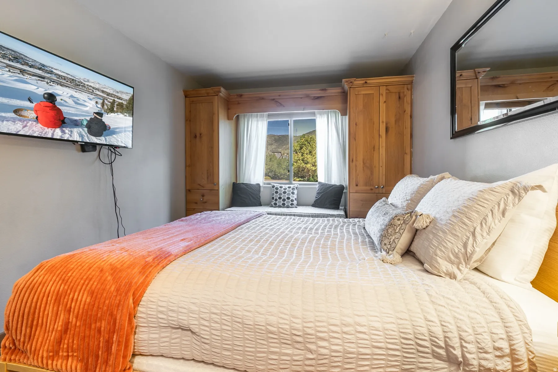 Bedroom featuring a built-in window seat, natural wood cabinetry, a wall-mounted television, and a large wall mirror