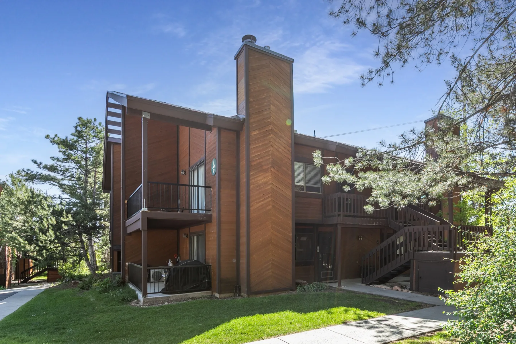 Multi-level exterior with wood siding, private balconies, an external staircase, multiple windows, and a prominent chimney feature