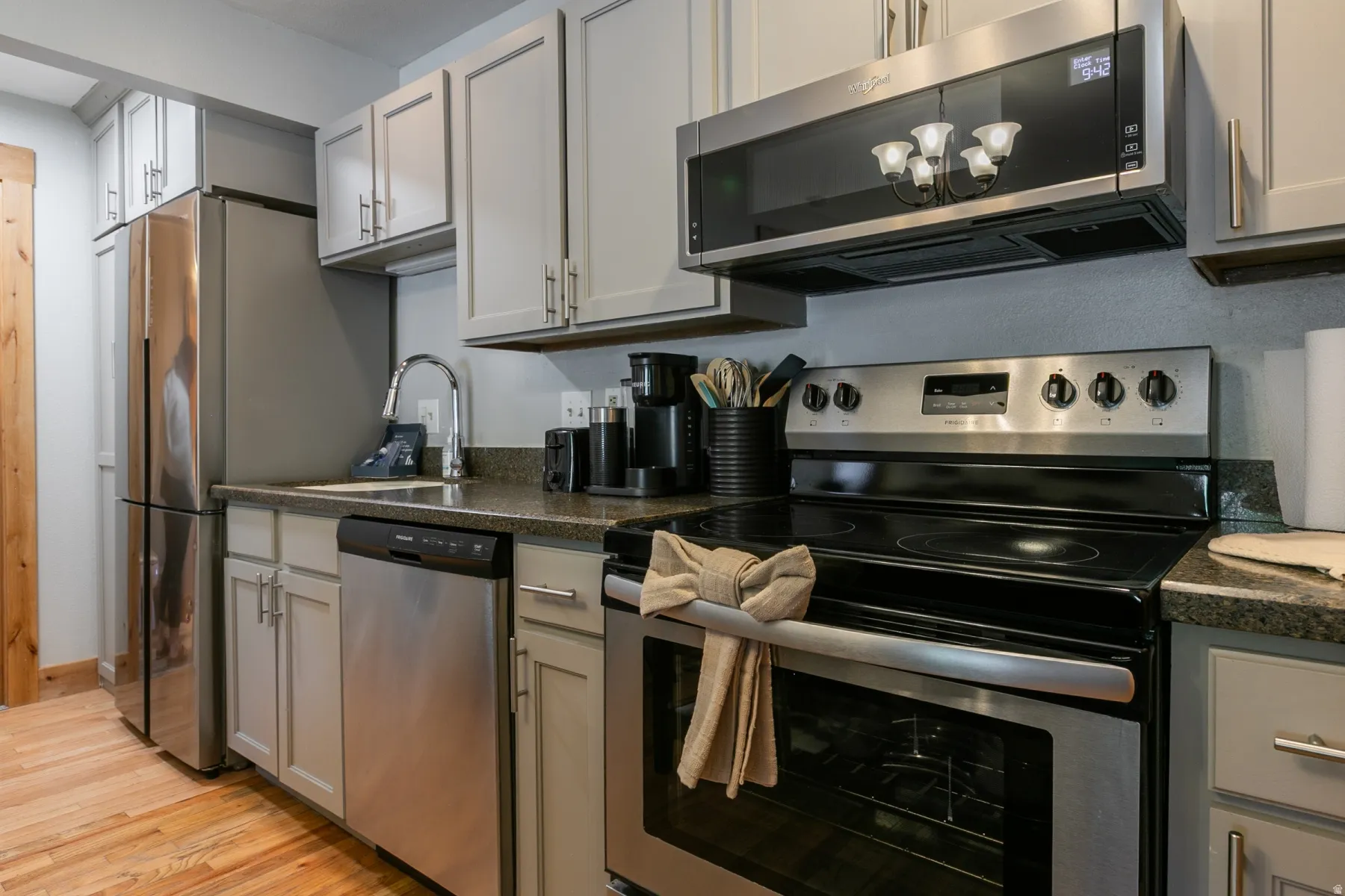 U-shaped kitchen featuring wood-finish flooring, stainless steel appliances, light gray cabinetry, dark speckled countertops, and a single basin sink with a gooseneck faucet