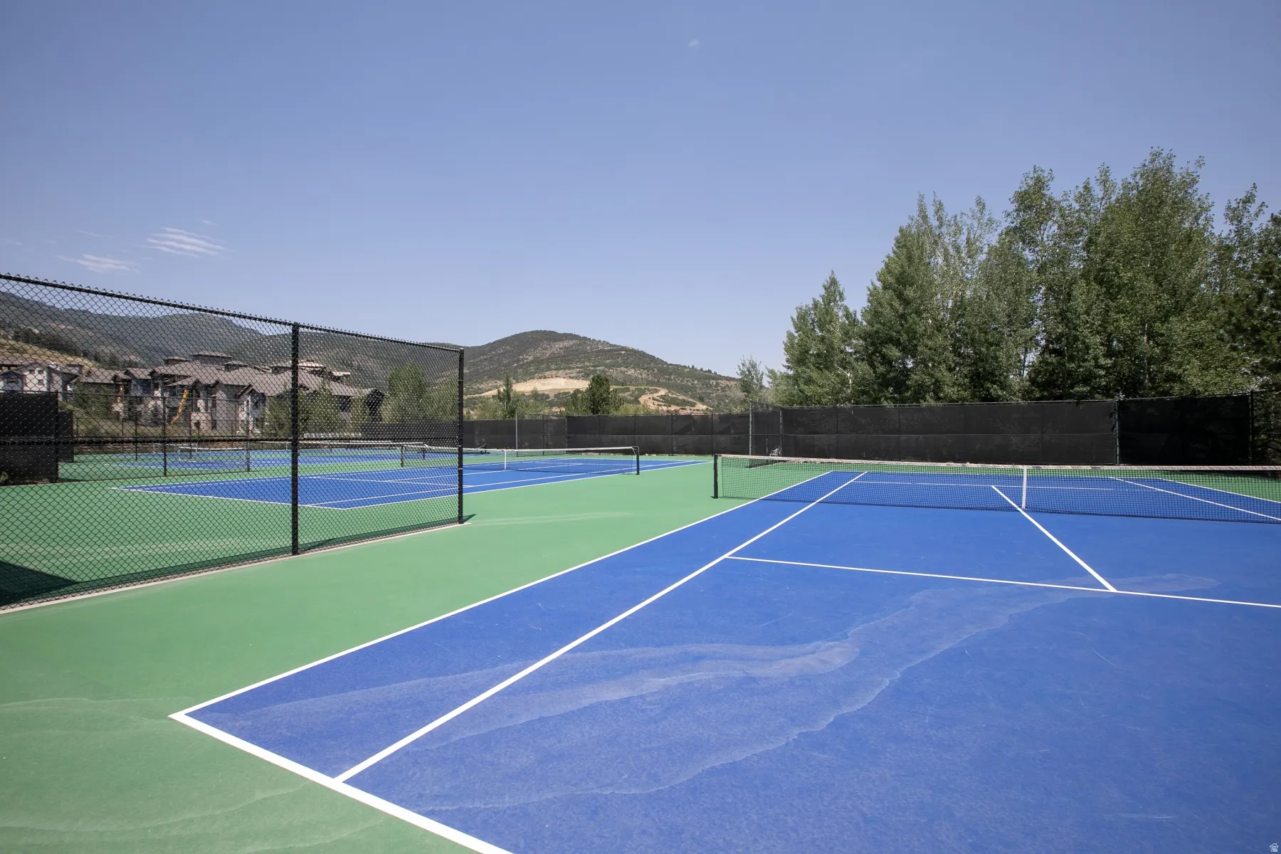 Multiple hard-surface tennis courts featuring blue playing areas and green surrounds