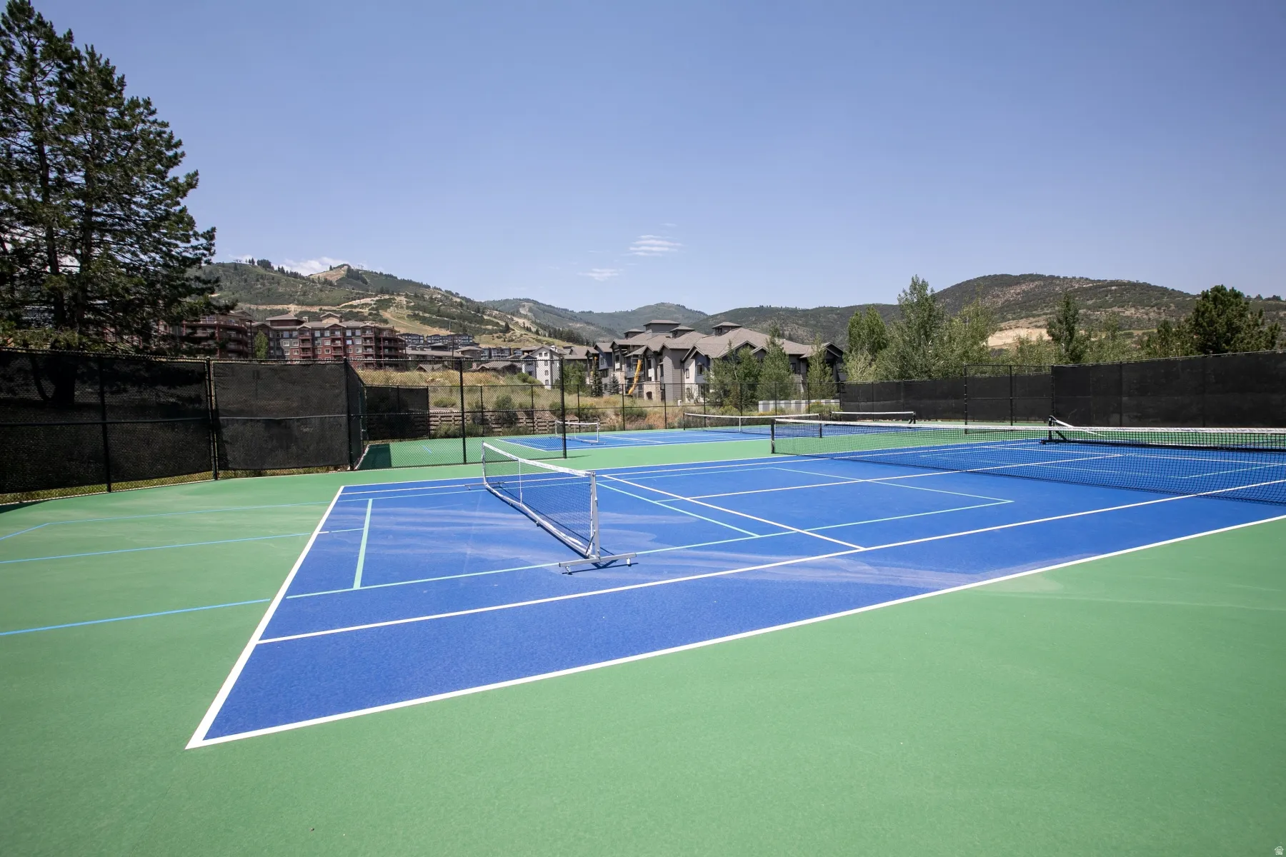 Two hard tennis courts featuring vibrant blue playing surfaces and green surrounds