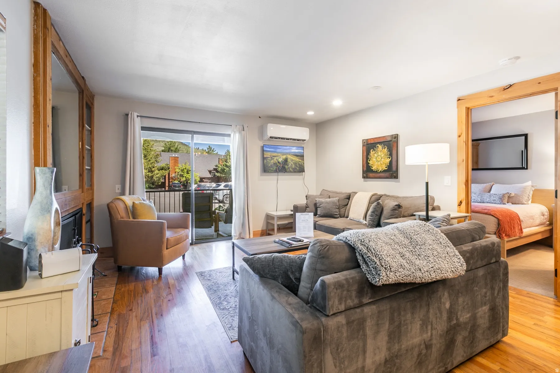 Open-concept living space with wood-finish flooring, a wall-mounted climate control unit, and recessed lighting