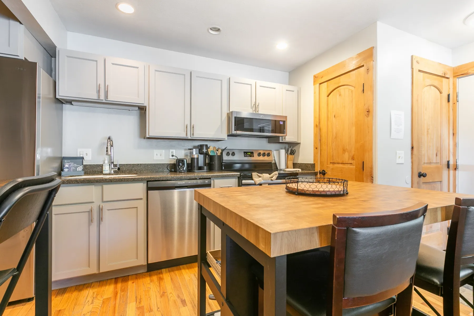 Kitchen featuring light gray cabinetry, stainless steel appliances, dark countertop, wood-finish flooring, and a butcher block island