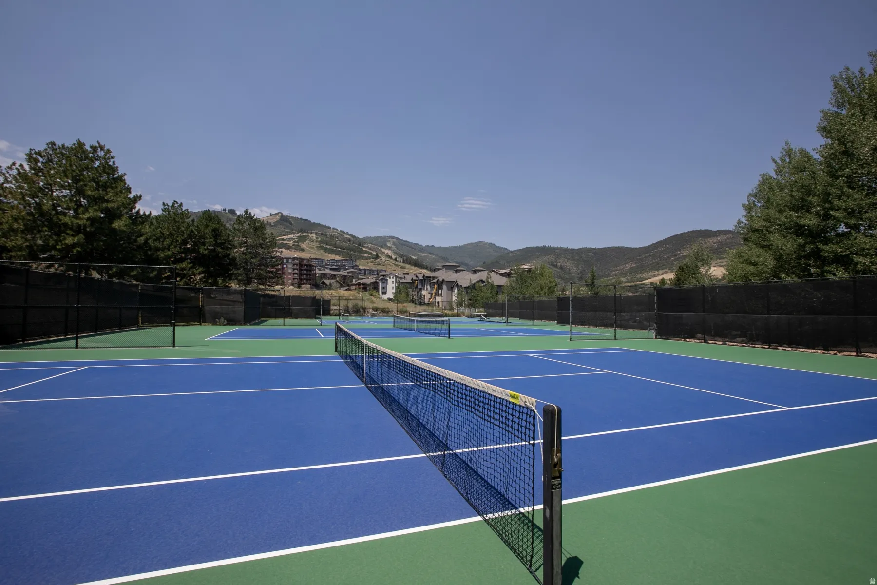 Multiple blue and green tennis courts with black perimeter fencing
