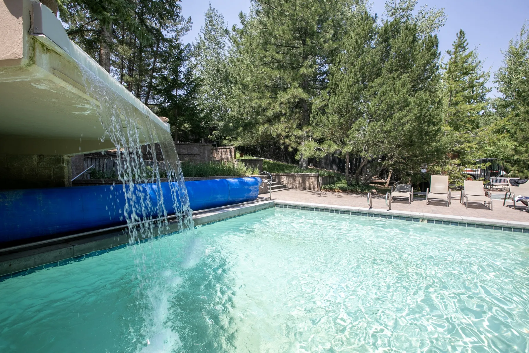 Outdoor swimming pool with a stone waterfall feature, surrounding green tile coping, and a concrete deck