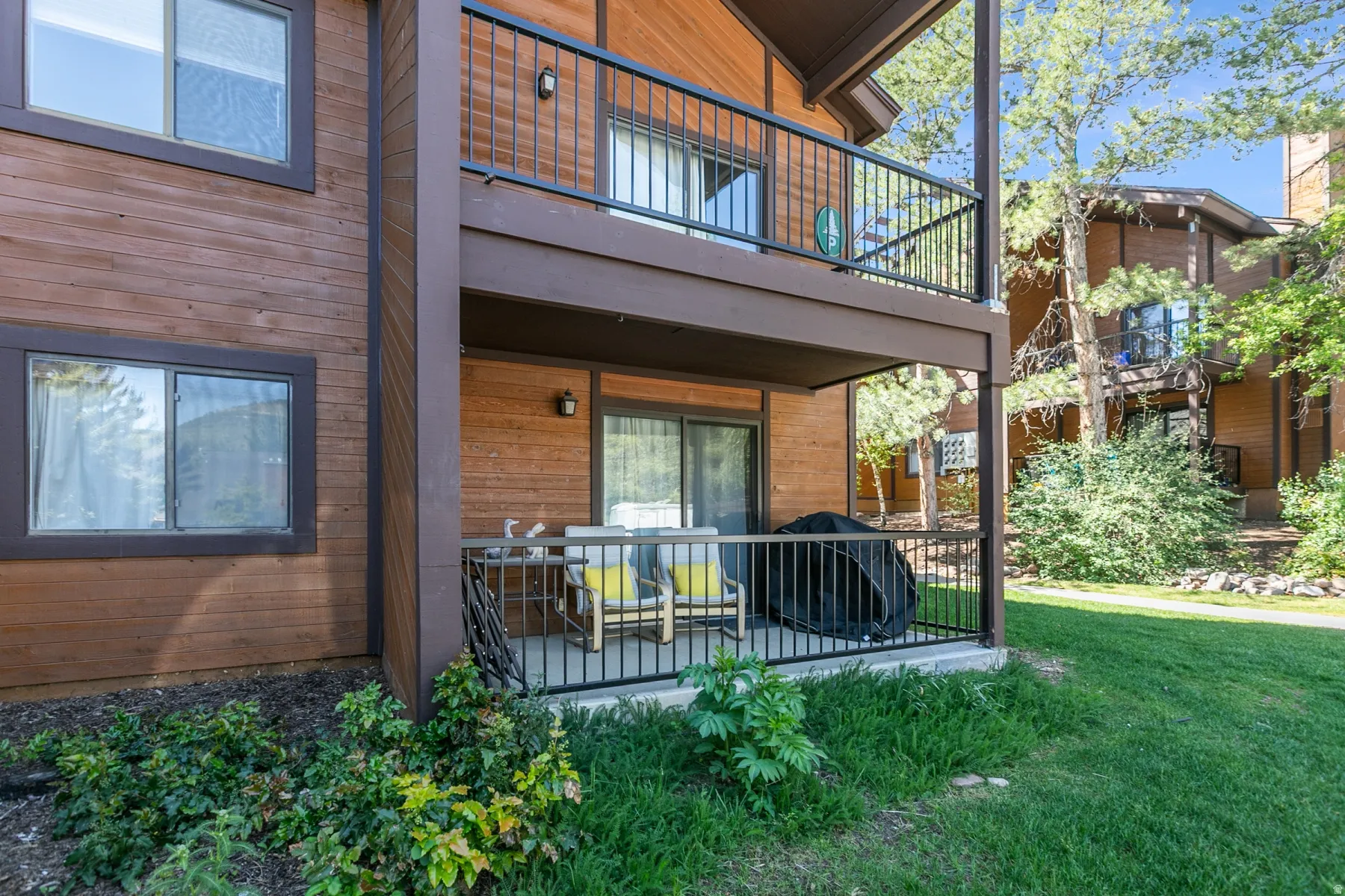 Wood-finish exterior featuring a ground-level patio and an upper-level balcony, both with dark metal railings