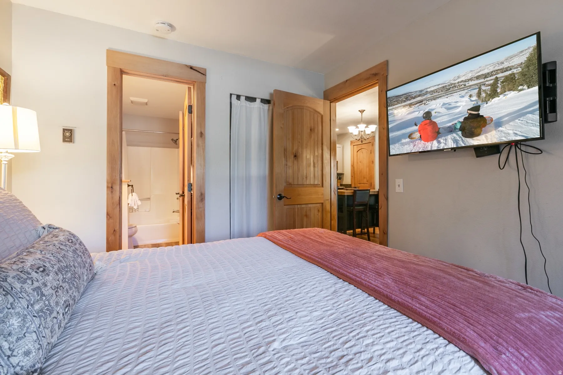 Wall-mounted television with visible access to a bathroom featuring a shower-tub combination, and an additional room with a bar-height counter