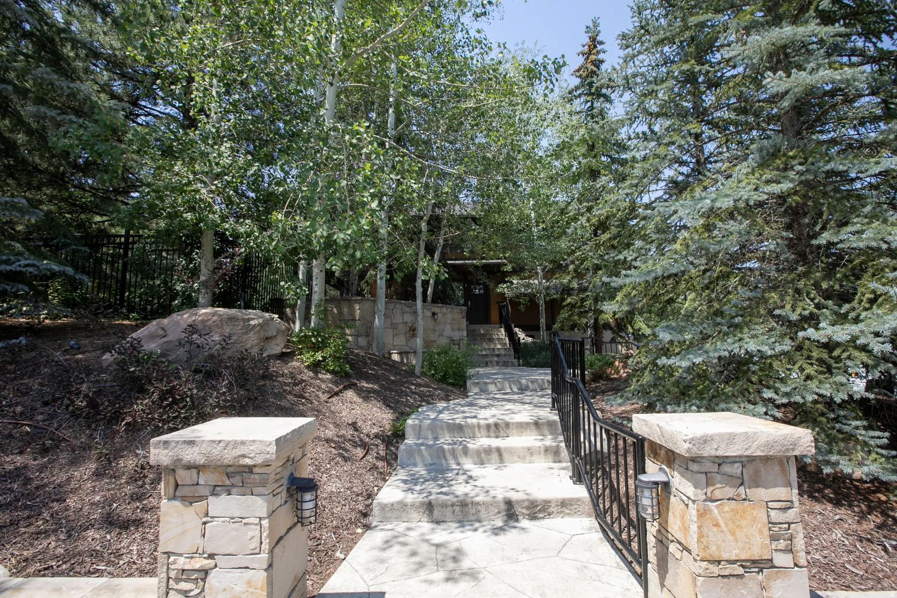 Stone entry pillars with integrated lighting and a black metal railing border a stone staircase leading to the property entrance