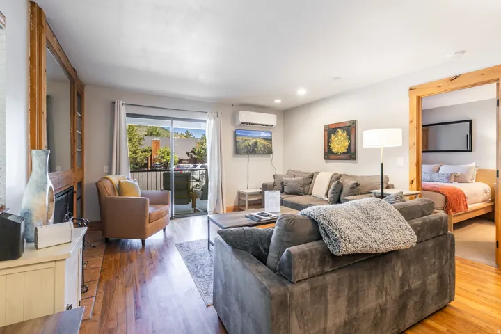 Open-concept living space with wood-finish flooring, a wall-mounted climate control unit, and recessed lighting