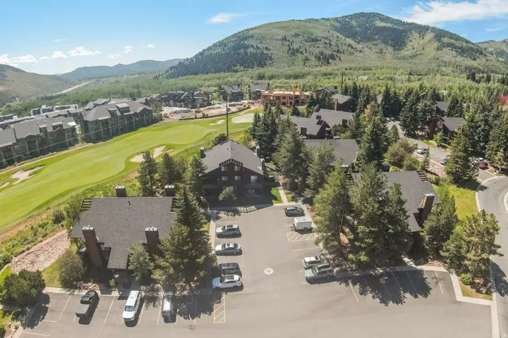 Aerial perspective showcasing multiple residential buildings with dark roofs and light-colored siding, surrounded by mature evergreen trees