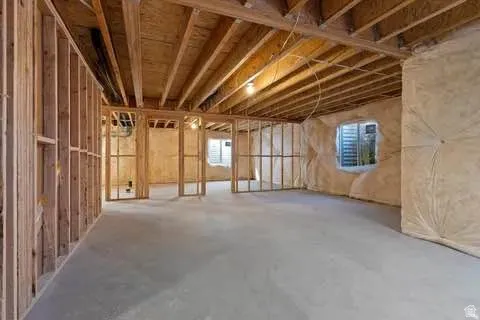 Unfinished basement featuring wood framing, exposed ceiling joists, concrete flooring, two egress windows, and insulation