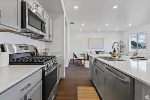 Kitchen featuring light gray cabinetry, stainless steel appliances, light-toned countertops, a gas range with an overhead microwave, and wood-finish flooring